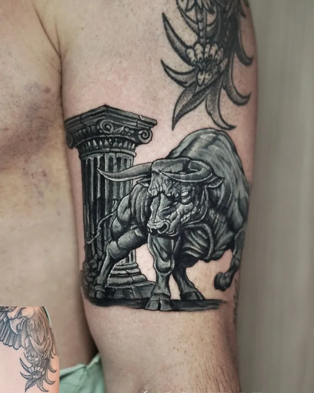 Black and grey charging bull with a Greek column, a cover-up tattoo on the upper arm