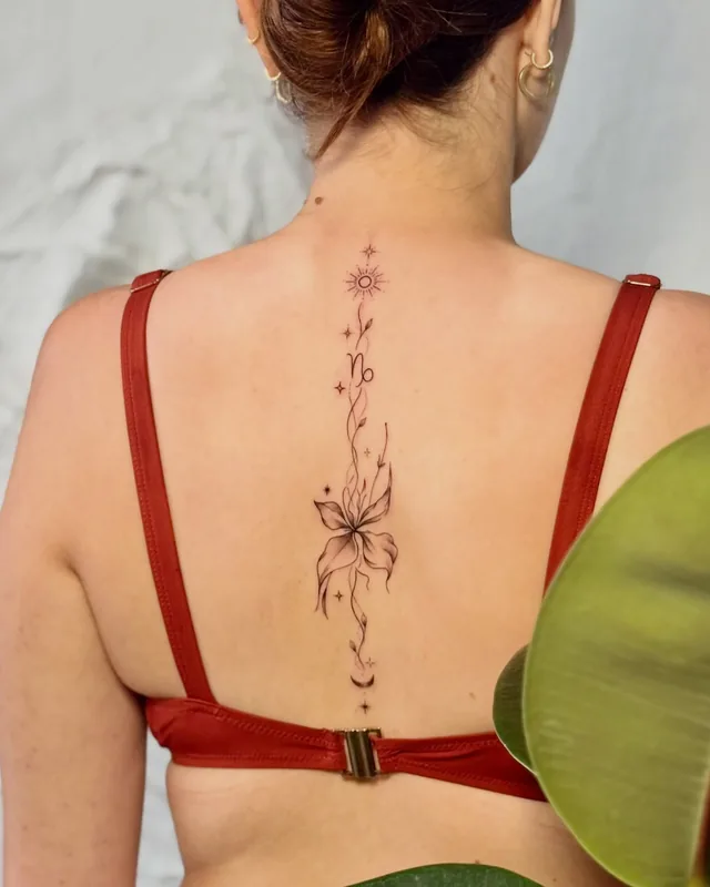 Fine line floral spine tattoo with a lily and small stars