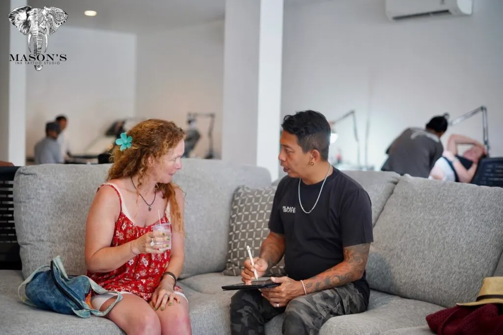 Tattoo artist sketching ideas with a client on the sofa at Mason's Ink